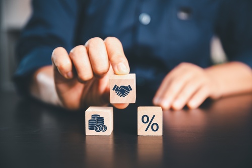 Person arranging wooden blocks displaying interest rate, money and handshake symbols, illustrating discretionary commission arrangements in car finance.